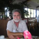 A man with white beard sitting at a table.