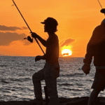 Two people fishing at sunset on the beach.