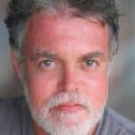 A man with grey hair and beard wearing a gray shirt.