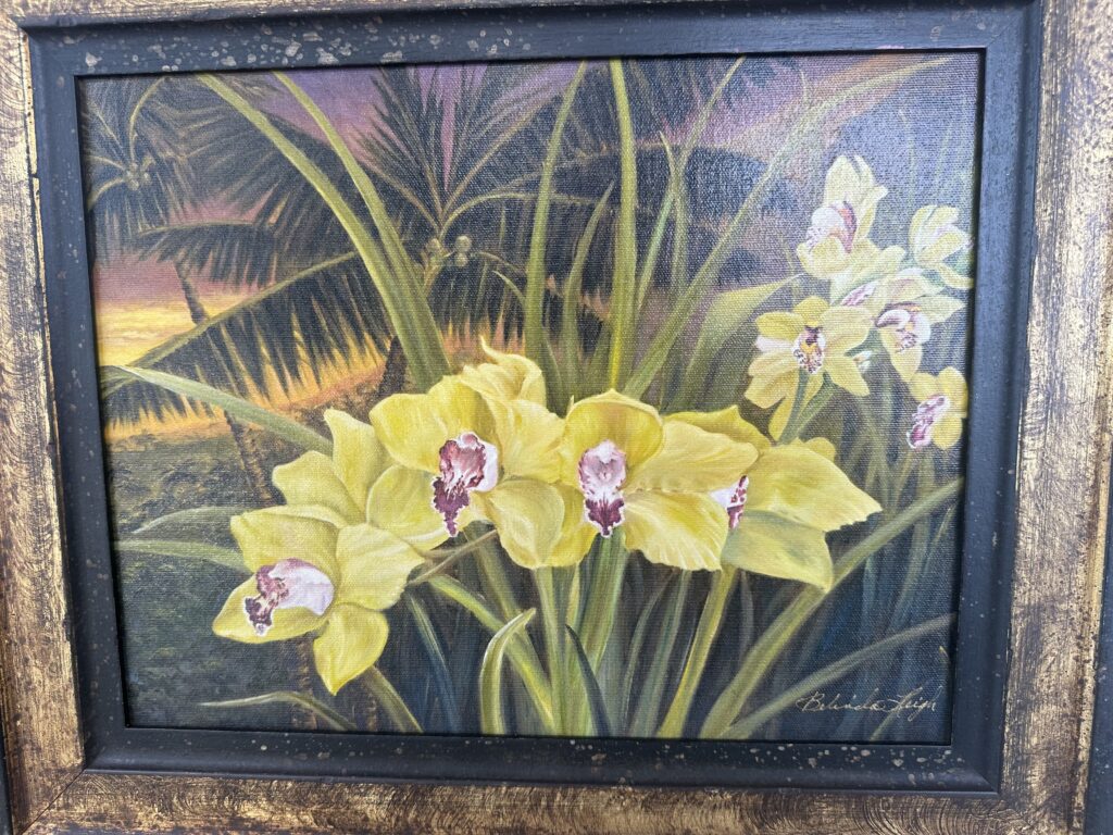 A painting of yellow orchids with green leaves and a dark frame.